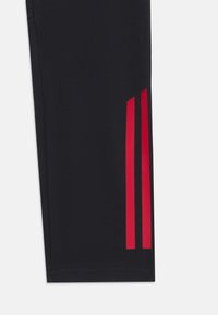 Svarte treningsbukser med r�øde tre-striper på siden, laget av elastisk materiale, med en glatt tekstur og en avsmalnende form.