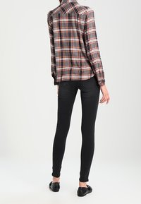 Camicia di flanella a quadri nelle tonalità grigio, nero e arancione, abbinata a jeans skinny neri e scarpe flat nere. Vista da dietro.