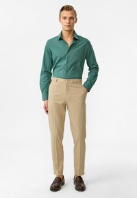 Groene blouse met lange mouwen, gecombineerd met lichtbeige slim-fit pantalon. Bruine leren loafers maken de outfit compleet.