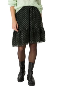 Jupe noire à volants avec un subtil motif floral vert, fabriquée à partir d'un matériau léger, associée à des bottines noires.