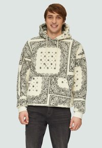 Fleece-Hoodie mit einem weißen und schwarzen geometrischen Muster, ausgestattet mit einer Kordelzugkapuze und gerippten Bündchen, kombiniert mit dunklen Jeans.