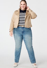 Beige motorjas van kunstleer, gestreepte marineblauwe en witte trui, lichtblauwe spijkerbroek en witte instapschoenen met uitsnijdingen.