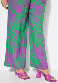 Pantaloni a gamba larga di un vivace viola, con un motivo floreale verde; abbinati a scarpe con tacco a blocco viola con fasce incrociate.