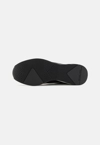 Semelle en caoutchouc noir de chaussure avec des rainures multidirectionnelles et des motifs triangulaires, avec le logo "Michael Kors" au talon.