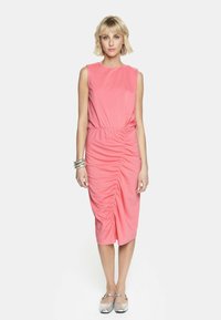 Różowa, bezrękawnikowa sukienka o marszczeniu, dopasowana w talii, z długością do kolan i miękką fakturą. Nosi ją z srebrnymi płaskimi butami i metalicznymi bransoletkami.