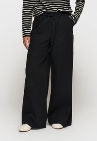 Zwarte wijde pijpenbroek met een koord in de taille, gemaakt van een soepele stof. Gecombineerd met een zwart-wit gestreept shirt met lange mouwen.