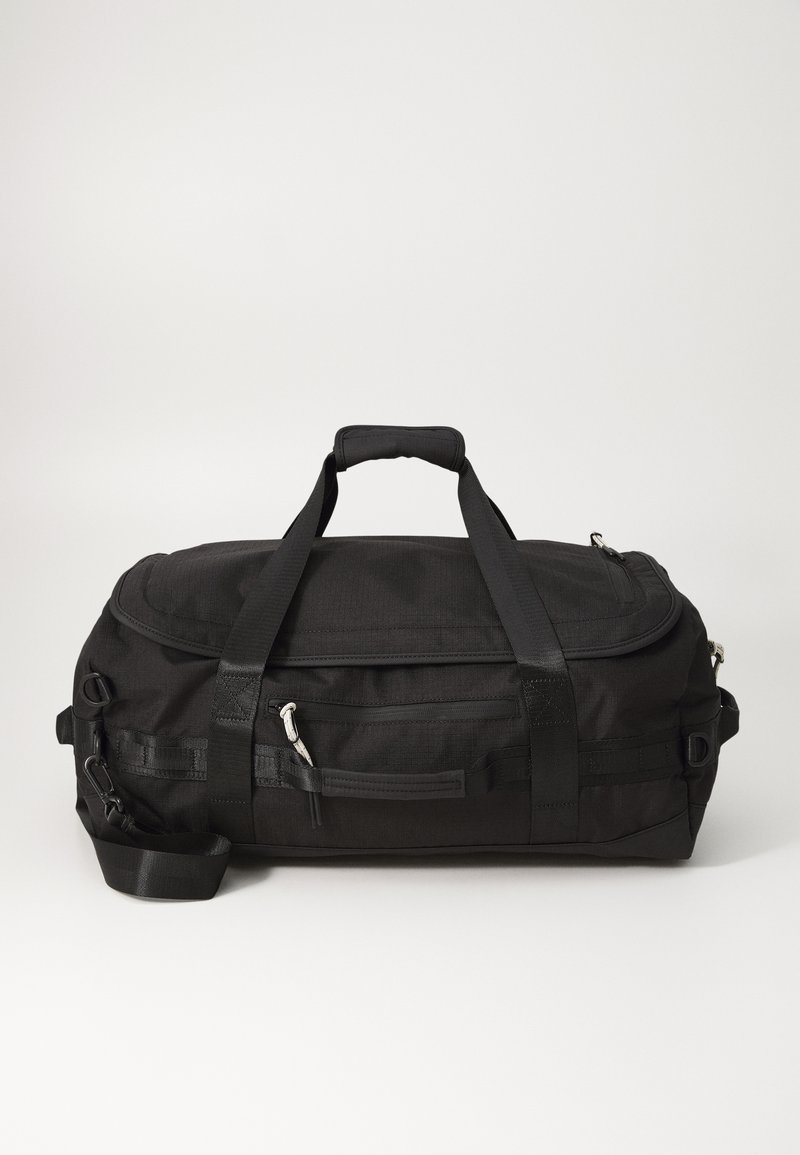 Sort duffle bag lavet af tekstureret stof, der har dobbelte håndtag, en aftagelig skulderrem og en frontlomme med lynlås til opbevaring.