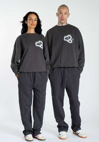 Dark gray sweatshirt and pants set, featuring a prominent white printed design on the chest, with visible stitching and relaxed fit.