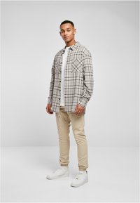 Grijze en witte geruite shirt met twee borstzakken, gecombineerd met beige broek en witte sneakers. Het shirt heeft een knoopsluiting.