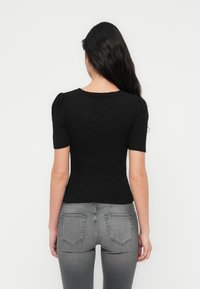 Μαύρο ριμπ κοντομάνικο τοπ με στρογγυλεμένη λαιμόκοψη και φουσκωτά μανίκια, συνδυασμένο με εφαρμοστά γκρι τζιν με τσέπες στην πίσω πλευρά.