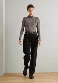 Haut col roulé avec un motif rayé ondulé en gris et noir, associé à un pantalon noir taille haute et des chaussures noires massives.
