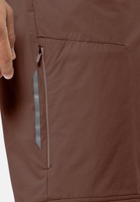 Des shorts en tissu marron avec une texture lisse présentent une poche zippée sur le côté et des éléments réfléchissants le long de la poche.
