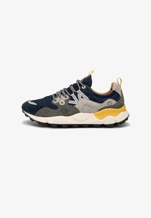 Zapatillas deportivas que combinan gamuza y malla en tonos azul marino, gris y beige, con una suela amarilla, acentos texturizados y cordones redondos.