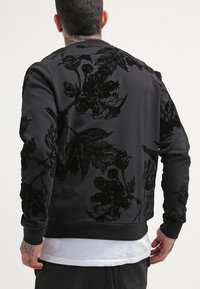 Svart sweatshirt med en blommig sammetstextur på baksidan, ribbade ärmslut och nederkant samt rundad halsringning.