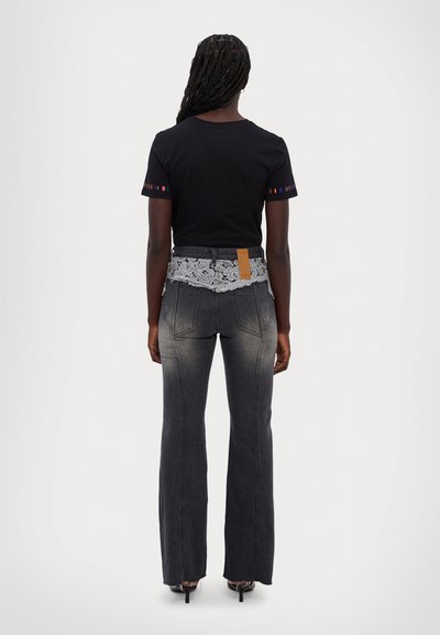 Svart t-shirt med färgglada detaljer på ärmarna, kombinerad med grå utsvängda jeans med spetsmidja och en beige etikett på baksidan.