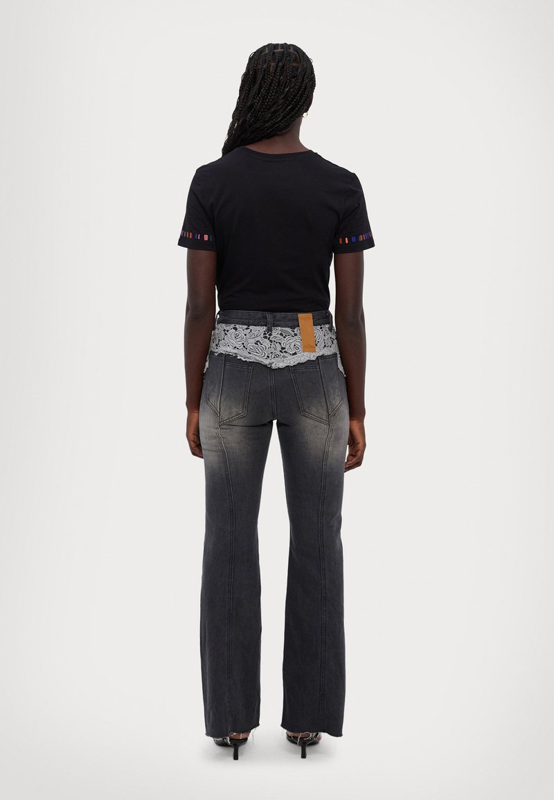 Zwarte T-shirt met kleurrijke accenten op de mouwen, gecombineerd met grijze flared jeans met een kanten tailleband en een beige label op de achterkant.