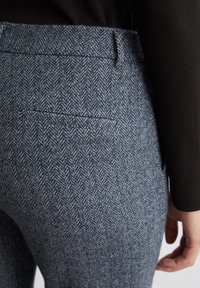 Pantalon ajusté en motif pied-de-poule bleu, présentant une texture lisse, taille mi-haute et un détail de poche arrière dissimulé.
