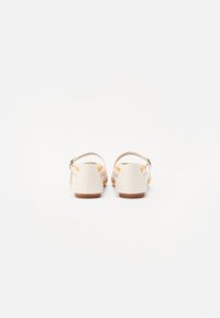Hvite sandaler med teksturert, stripet design i myke oransje og rosa nyanser, med en bakre stropp og trehelsdetaljer.