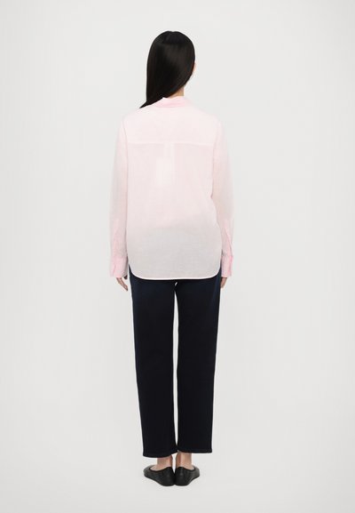 Chemise à manches longues rose clair avec une couture au dos, des poignets à boutons et une coupe décontractée, associée à un jean droit noir et des ballerines noires.
