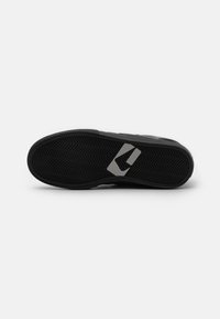 Suela de zapato atlético negra con patrón de espiga, con un destacado acento de logo gris y goma texturizada para mayor agarre.