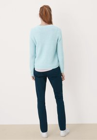 Pull tricoté bleu clair avec un motif texturé, associé à un pantalon slim bleu foncé et des baskets blanches. Encolure et poignets côtelés visibles.
