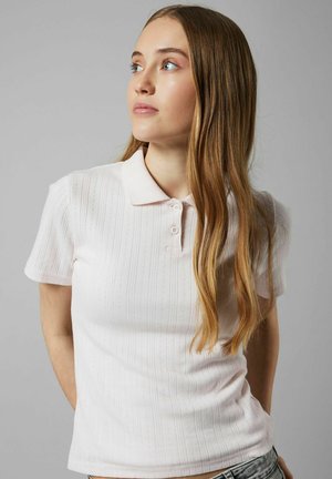 Polo en rose clair, à manches courtes, avec de légères rayures verticales et un col classique à trois boutons. Texture douce.