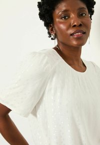 Weiße Bluse aus strukturiertem Material mit dezenten silbernen Akzenten, kurzen Puffärmeln, rundem Ausschnitt und gefaltetem Designdetail.