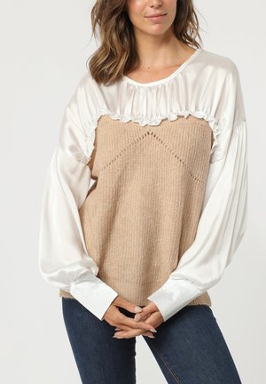 Suéter de punto beige con mangas globos de satén blanco y cuello con volantes; presenta un patrón texturizado y puños abotonados.