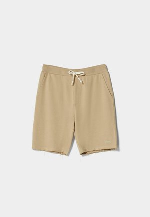 Beige Shorts in mittlerer Länge mit Tunnelzugbund und Seitentaschen, mit rohen Saumkanten und kleinem Logo am unteren Bein.