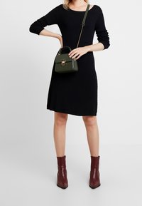 Czarna ribbed sukienka z długimi rękawami, w połączeniu z małą zieloną torebką z zapięciem w kolorze złotym oraz burgundowymi botkami za kostkę.