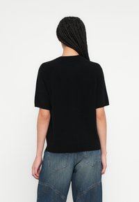 Μαύρο πουλόβερ με κοντά μανίκια και στρογγυλή λαιμόκοψη, κατασκευασμένο από λείο και απαλό ύφασμα. Διαθέτει άνετη εφαρμογή και ριμπ τελείωμα στο στρίφωμα.