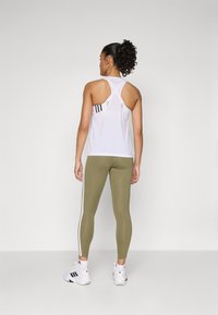 Top atletico bianco con design a racerback, leggings verde oliva con strisce laterali bianche e scarpe da ginnastica bianche.