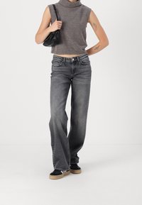 Harmaa hihaton korkea kauluspaita, korkeavyötäröiset harmaat farkut, joissa on liehukkeet, musta-valkoiset lenkkarit, pitäen pientä mustaa käsilaukkua.