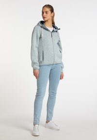 Jasnoniebieska bluza z kapturem na zamek, z regulowanym kapturem, ściągaczami przy rękawach i bocznymi kieszeniami, w połączeniu z jasnoniebieskimi skinny jeansami i białymi trampkami.