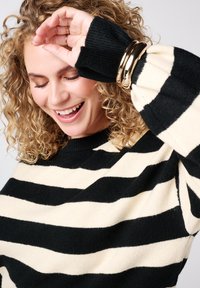 Pull rayé noir et crème ; manches longues avec poignets côtelés et encolure décontractée ; tissu en maille texturée.