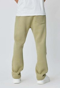 Pantalons de survêtement décontractés, de couleur vert clair, avec une taille élastique, des poches latérales et une poche arrière unique. Texture lisse ; poignets côtelés.