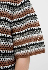Blouse au crochet à manches courtes avec des rayures alternées de marron, noir, blanc et des détails texturés. Design à mailles ouvertes.