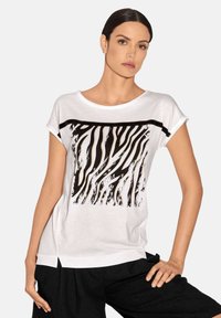 Weißes T-Shirt mit kurzen Ärmeln, das ein schwarz-weißes Zebra-Streifen-Design über der Brust aufweist, mit einem abgerundeten Halsausschnitt und seitlichen Schlitzen.
