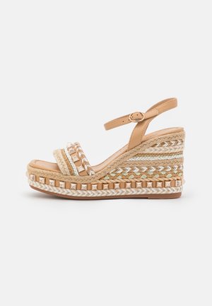 Kile-sandal i beige med ankelsrem og spænde, med flettede og vævede teksturdetaljer på platåsko.