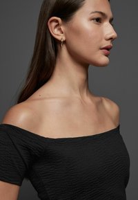 Top nero testurizzato scollato, caratterizzato da una silhouette aderente e maniche corte. Il modello indossa orecchini a cerchio dorati su uno sfondo neutro.
