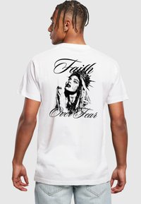 White short-sleeve t-shirt featuring a black graphic of a woman with a crown, praying, alongside the text "Faith Over Fear" in cursive.