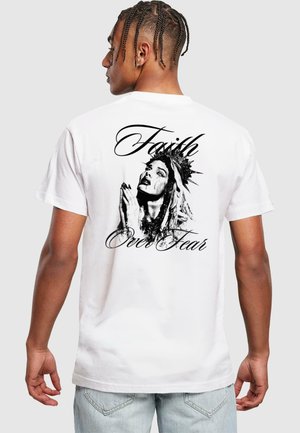White short-sleeve t-shirt featuring a black graphic of a woman with a crown, praying, alongside the text "Faith Over Fear" in cursive.