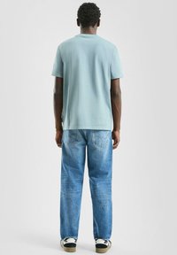 Jasnoniebieska bawełniana koszulka z krótkimi rękawami, zestawiona z wyblakłymi niebieskimi dżinsami. Widoczne przeszycia i dwie tylne kieszenie.