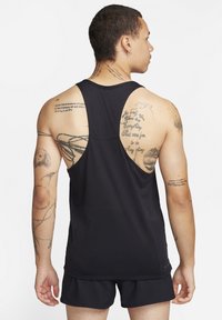 Schwarzes ärmelloses Tanktop mit rundem Halsausschnitt, aus strukturiertem Stoff und sportlichem Schnitt. Sichtbare Tattoos an den Oberarmen und im Rücken.