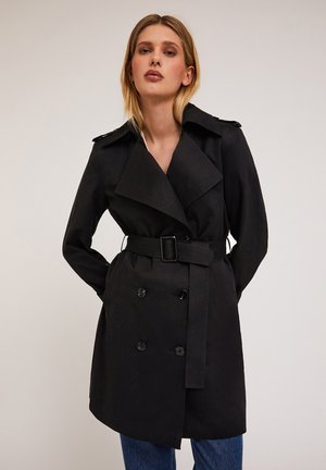 Manteau noir en trench-coat avec un design à double boutonnage, de larges revers, une taille ceinturée et des poches latérales. Fabriqué en tissu léger et lisse.