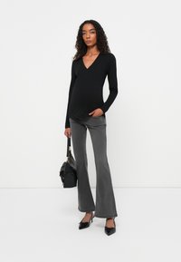 Top avvolgente a maniche lunghe nero abbinato a pantaloni grigi a zampa. Borsa nera con hardware dorato, tacchi appuntiti neri. Texture lisce e design aderente.