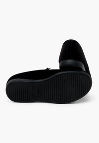 Black flats made of soft, textured material with a rounded toe and a low heel. The sole is flexible with a tread pattern for grip.
