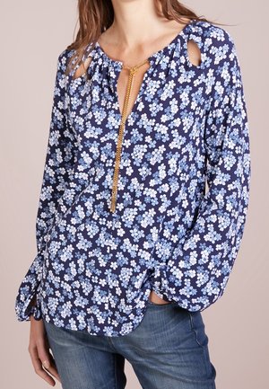 Marine-blaues Blumen-Bluse aus weichem Stoff, mit Blau- und Weiß-Blumenmustern, Rundhalsausschnitt mit goldener Kettendetail und langen Ärmeln.