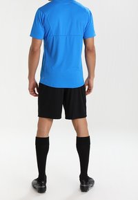 Blaues Sportshirt mit kurzen Ärmeln, kombiniert mit schwarzen Shorts und knielangen schwarzen Socken. Das Material wirkt leicht und atmungsaktiv.