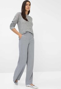 Grijze trui met een gestructureerde afwerking, gecombineerd met lichtgrijze broek met streepjes en zilveren flats, met een relaxte pasvorm en zakken.